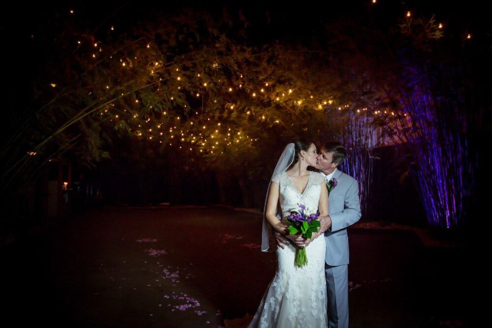 Nighttime Outdoor Bride and Groom Portrait at DTSP Wedding Venue NOVA 535 Bamboo Garden with Purple and Greenery Bouquet and Boutonnière, Groom in Gray Suit