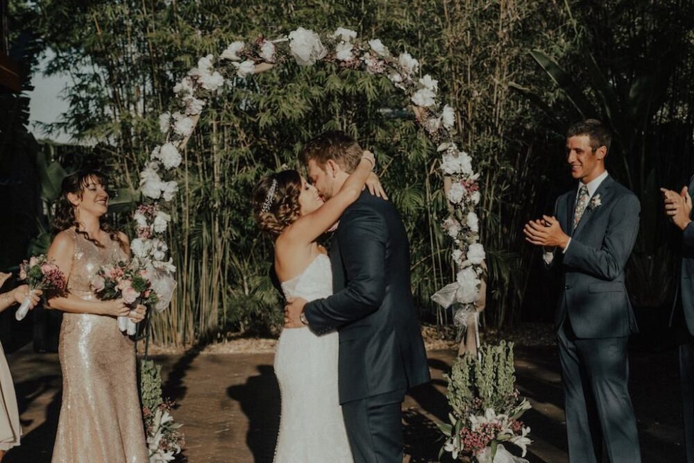 Bamboo Outdoor Courtyard Garden Wedding Ceremony Portrait, Groomsmen in Gray Suits with Floral Tie, Bridesmaids in Mismatched Blush and Rose Gold Dresses, with Rustic Bohemian Floral White Floral and Greenery Arch | Downtown St Pete Wedding Venue NOVA 535