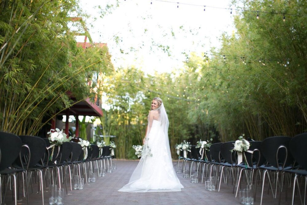 Bride with chapel veil at modern ceremony under string lights in bamboo garden at NOVA 535